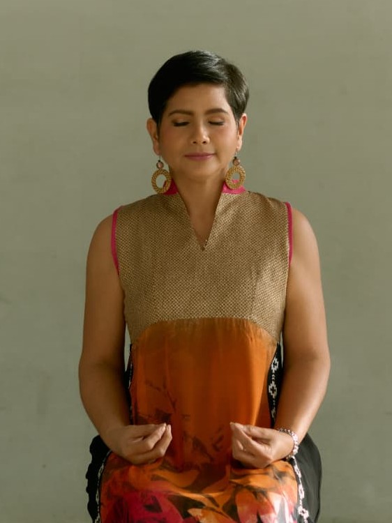 Angelica Umali seated with eyes closed in meditation, wearing a gold and amber dress