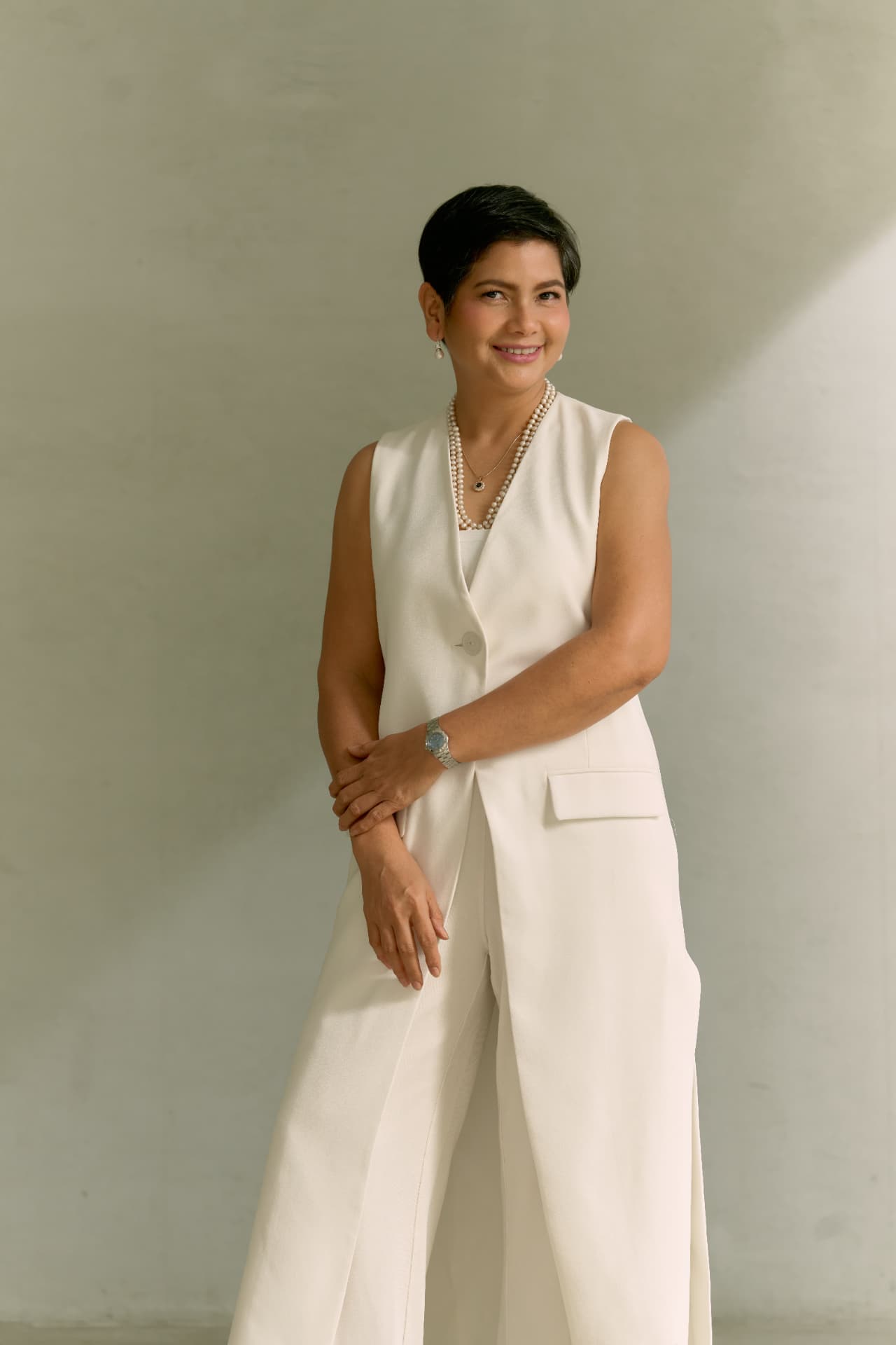 Angelica Umali smiling in a cream vest and pearls